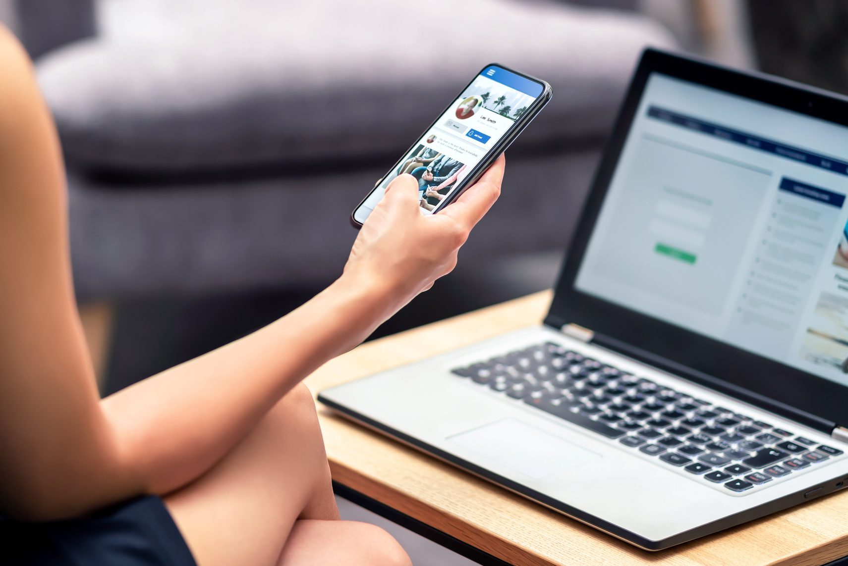 Social media profile page in smartphone screen at work. Woman looking at feed, status update or post with mobile phone. Inefficient lazy worker avoiding job.