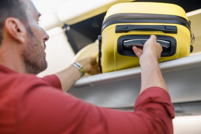 Man pulling out hand luggage from compartment while traveling by plane