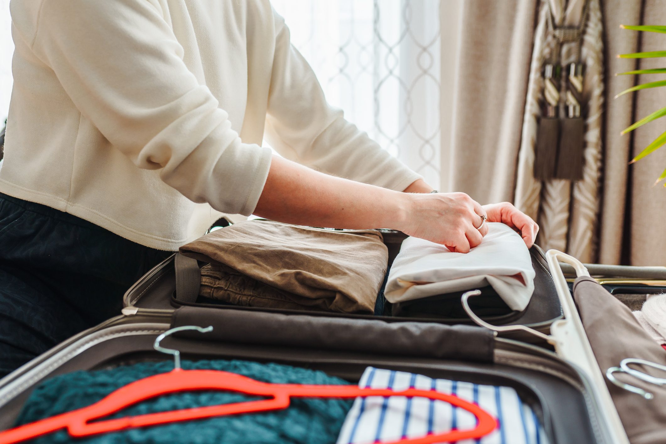 Close up hands of unrecognisable woman packing suitcase. Woman putting clothes inside of bag