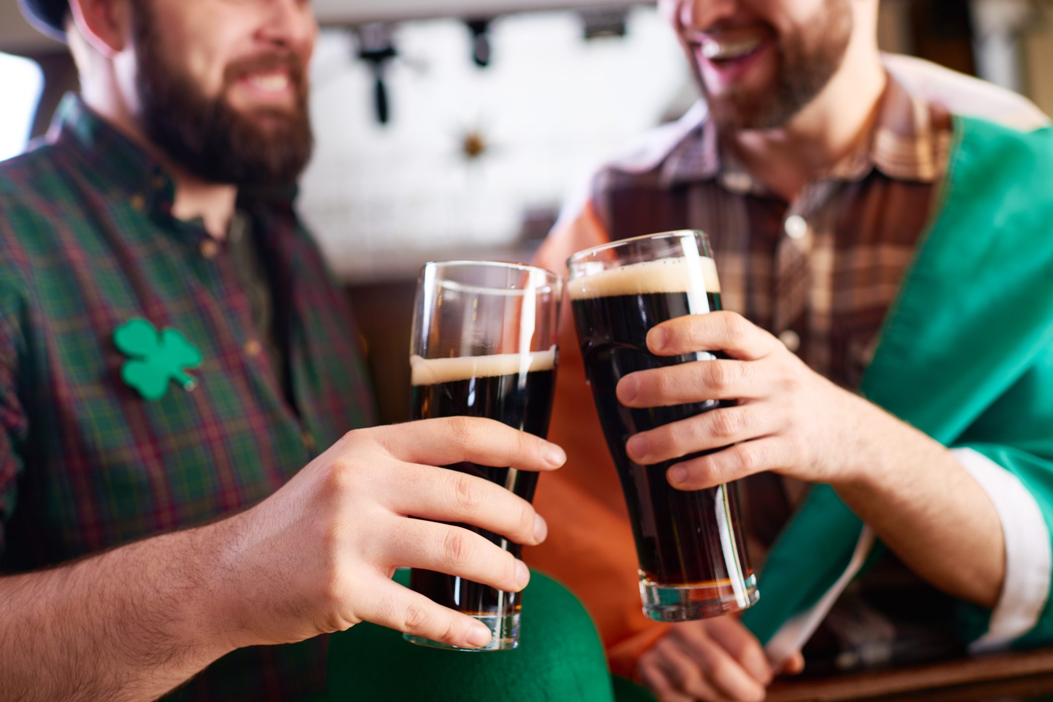 Two men clinking glasses of dark beer, smiling, in a festive setting with green and orange clothing.