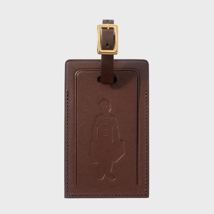 Brown leather luggage tag embossed with a figure, attached to a strap with a gold buckle, set against a plain background.