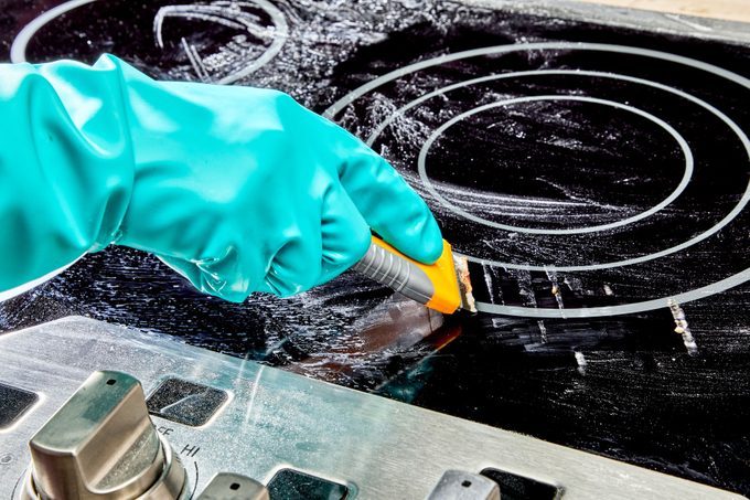 gloved hand using razor blade to scrape off burnt on food