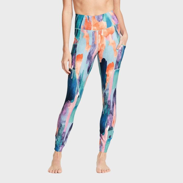Colorful leggings display a vibrant abstract pattern, worn by a person standing barefoot against a plain white background.
