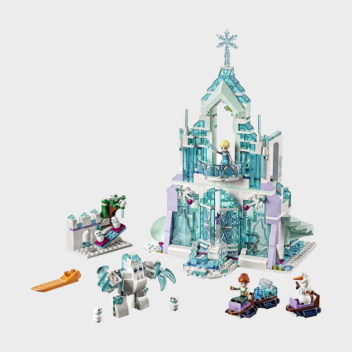 A toy ice palace with mini-figures stands surrounded by small characters and sleds, in a playful setting.
