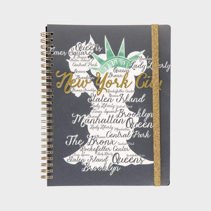 Notebook cover features the Statue of Liberty silhouette filled with handwritten New York City place names, adorned with a gold elastic band and spiral binding.