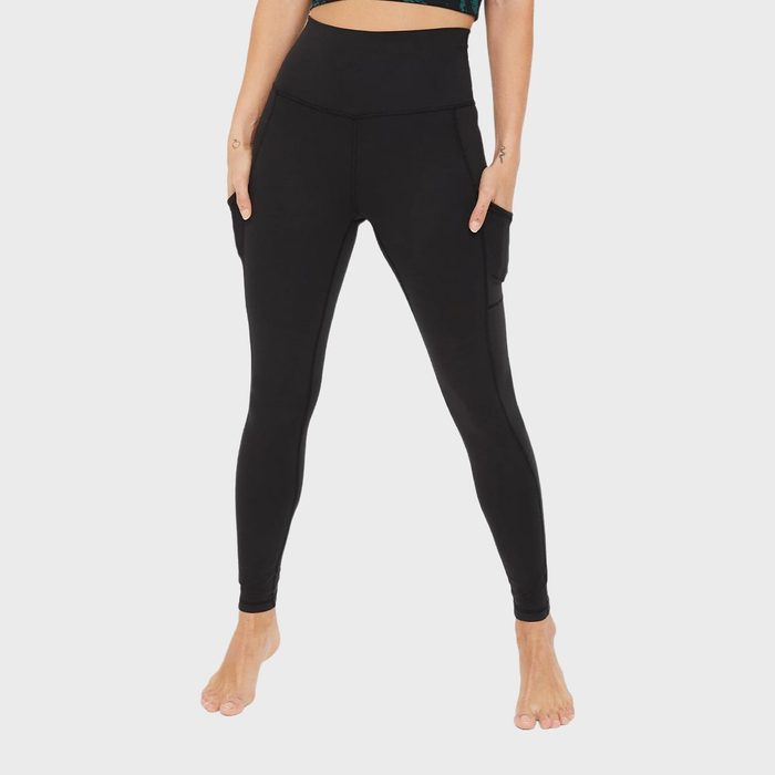 Person wearing black leggings stands barefoot with hands in pockets against a plain white background.