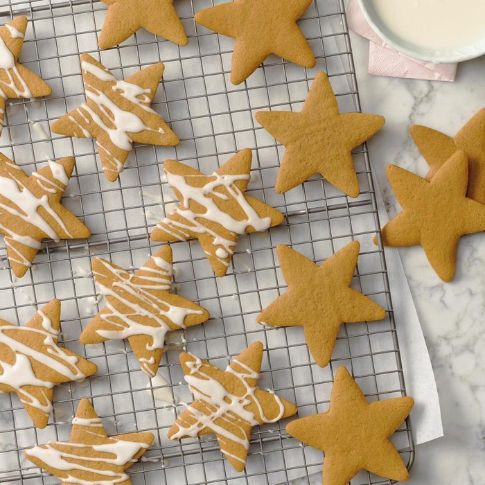 Star-shaped cookies cool on a wire rack; some are drizzled with white icing. They sit on a marble countertop.
