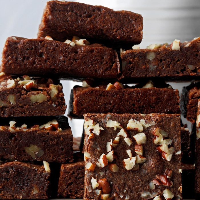 Brownie squares stacked with visible chopped nuts, displayed against a blurred light gray background.