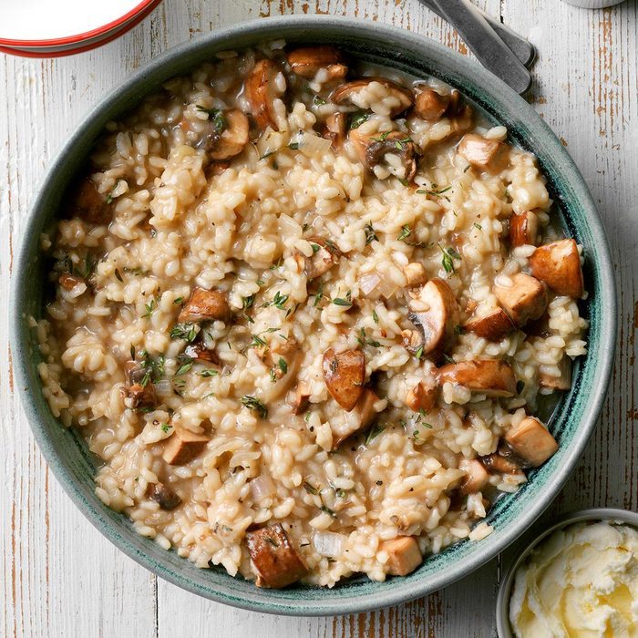 Creamy mushroom risotto fills a rustic bowl on a wooden table, accompanied by a small dish of butter and a fork nearby.