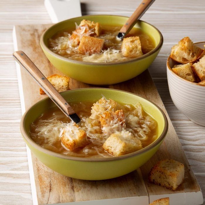 Bowls hold soup topped with croutons and cheese, placed on a wooden board. A side bowl contains extra croutons.