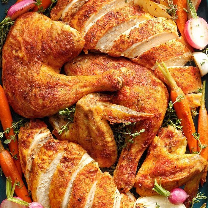 Roasted chicken pieces rest on a platter surrounded by carrots, radishes, and herbs, creating a colorful, appetizing display.
