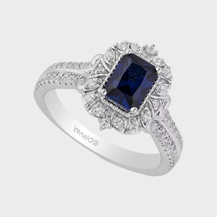 Ring features a large blue rectangular gemstone surrounded by small diamonds, resting on a silver band intricately designed; 