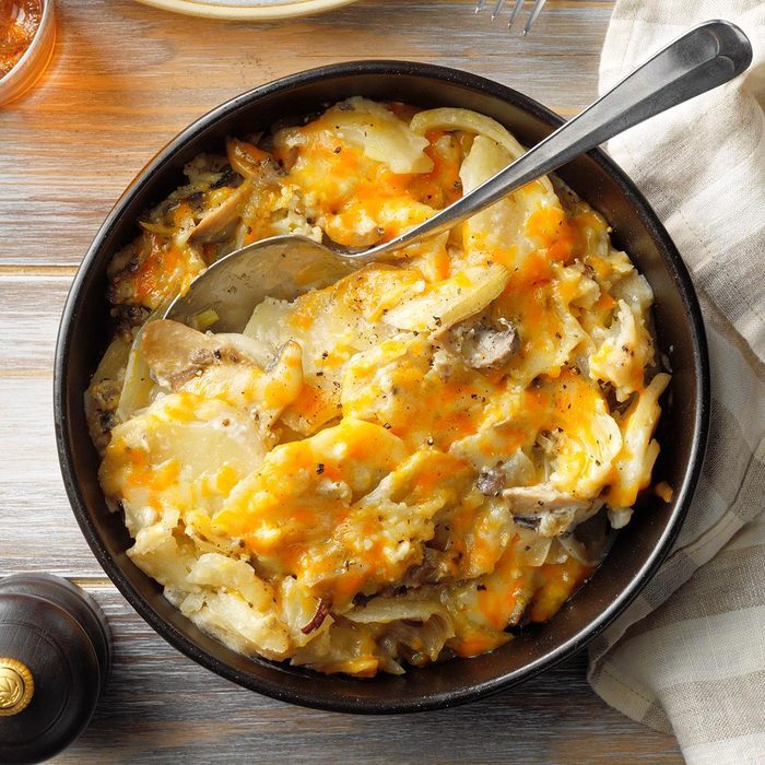 A bowl filled with cheesy scalloped potatoes sits on a wooden table with a spoon resting inside.