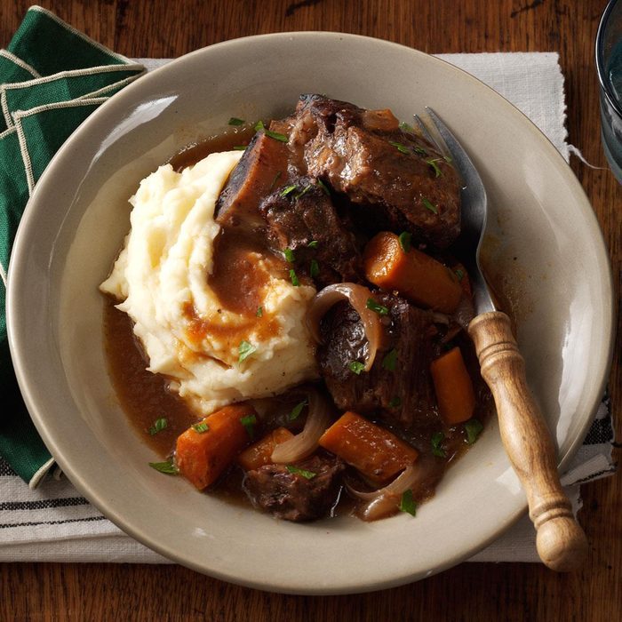 Plate holding mashed potatoes and beef stew sits on a wooden table, garnished with parsley and accompanied by a fork.