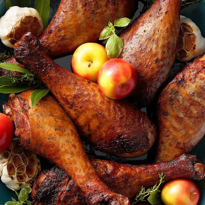 Roasted turkey legs rest among fresh apples, herbs, and whole garlic bulbs, creating an inviting and rustic culinary presentation.