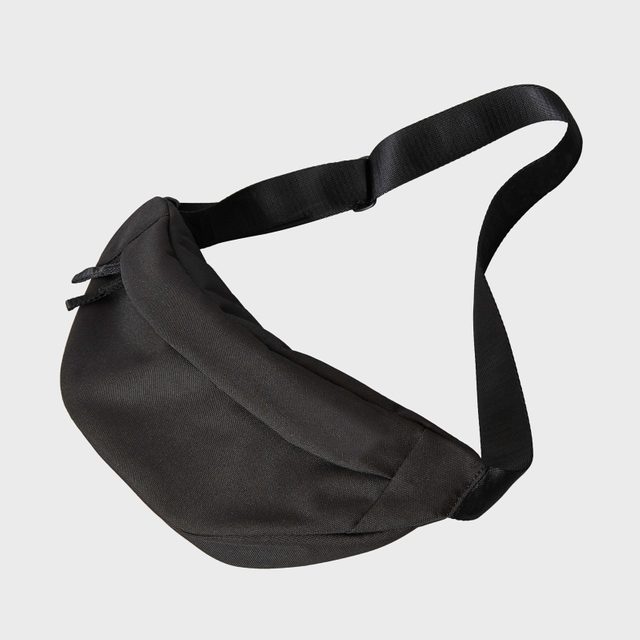 Black waist bag rests, strap extended, against a plain gray background.