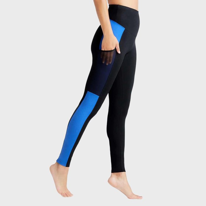 Legs wear black leggings with blue side panels, standing balanced on one foot against a plain grey background.