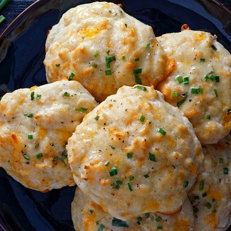 Cheese biscuits rest on a dark plate; sprinkled with chives, they display a golden, baked texture.