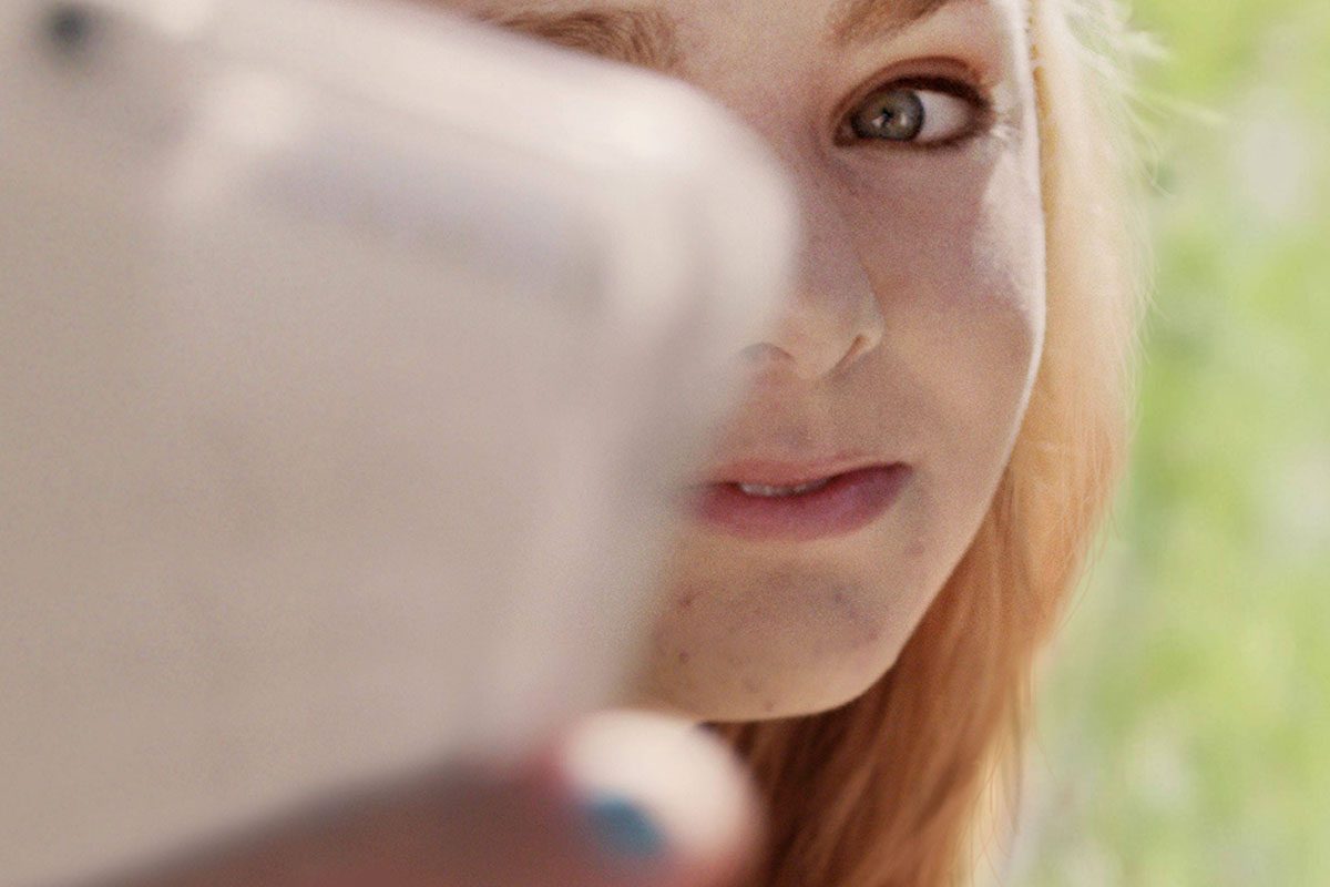 A person holds a phone, focusing on the screen, with a blurred green background outdoors.