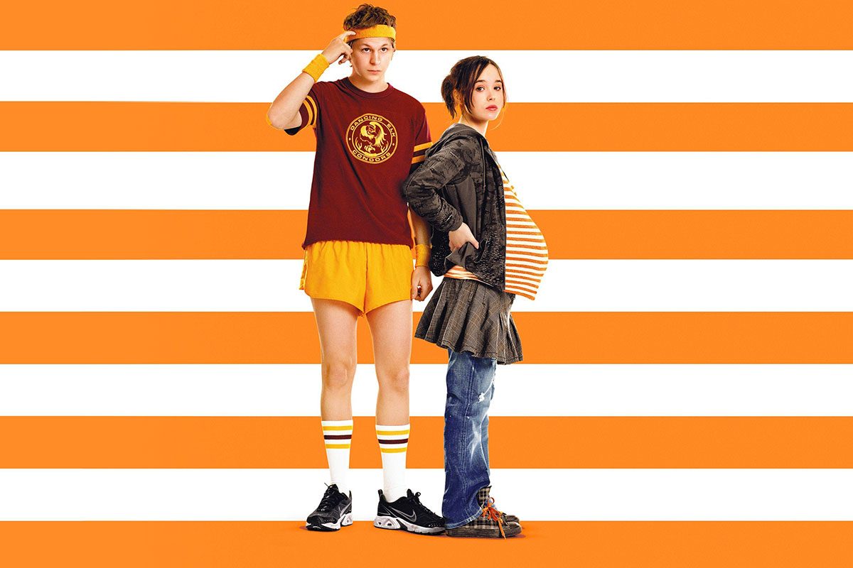 Two people stand back-to-back; one wears sportswear, the other is pregnant in casual attire, against a background of orange and white stripes.