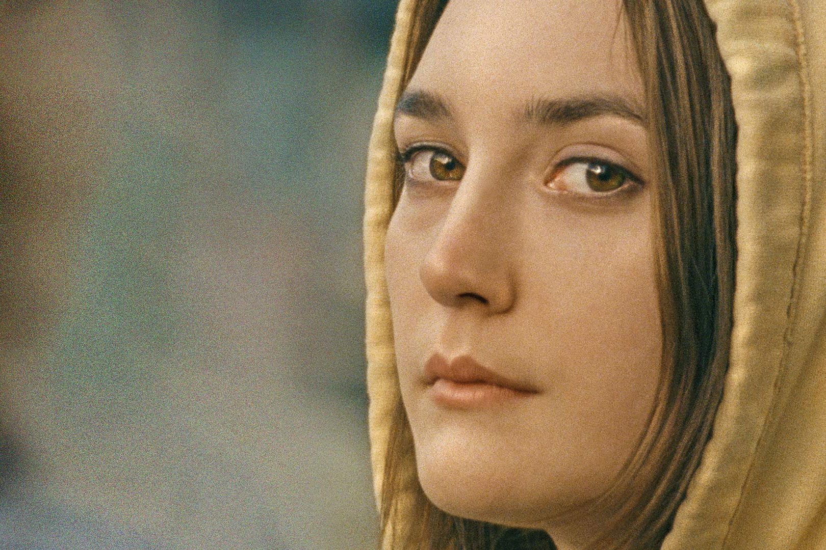 Person gazes calmly, wearing a yellow hoodie, with a blurred, neutral background.