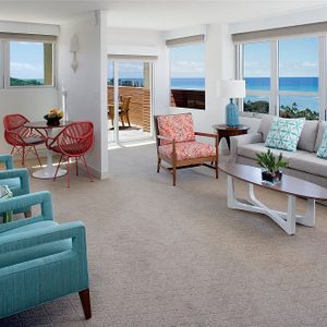 Living room features modern furniture with colorful seating and a wooden coffee table; large windows reveal ocean views and a balcony.