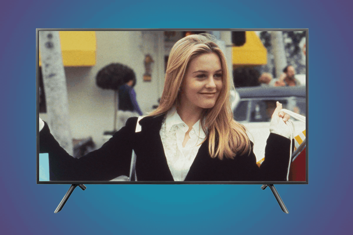 A television displays a smiling individual with long blonde hair outdoors, against a background of people, cars, and buildings.