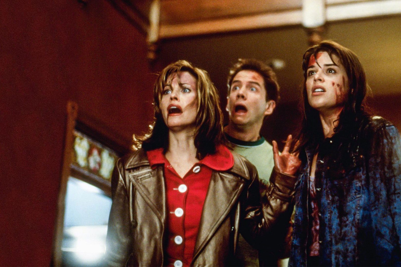 Three people stand scared, covered in blood, in a dimly lit room with wooden beams and stained glass.