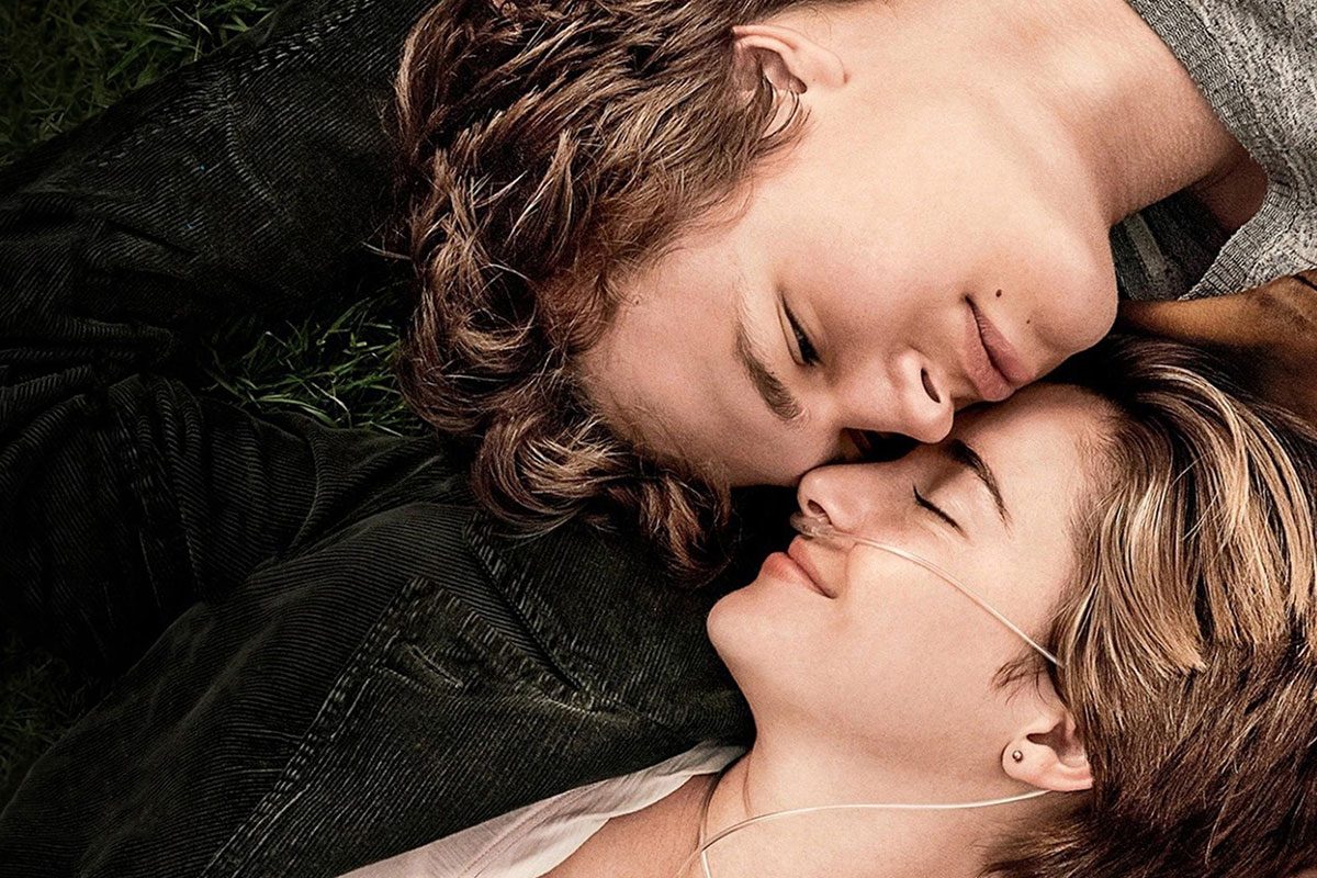 Two people lie closely together, eyes closed, on green grass, sharing earphones.