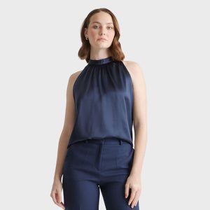 Person standing wearing a sleeveless navy blouse and matching trousers, with short brown hair, set against a plain light background.