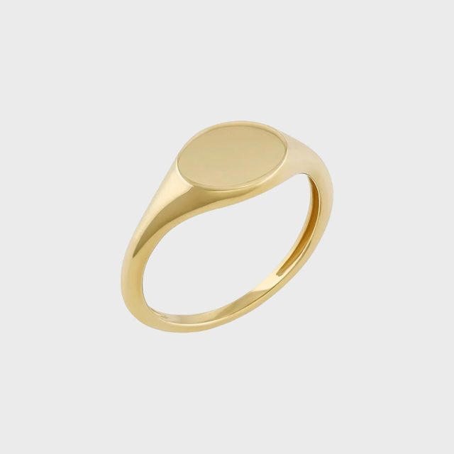 A gold ring with a flat, circular top, displayed on a plain gray background.