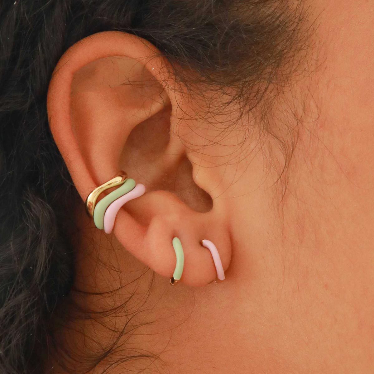 Ear displays colorful, wavy earrings and a gold cuff; hair partially visible surrounding the ear.