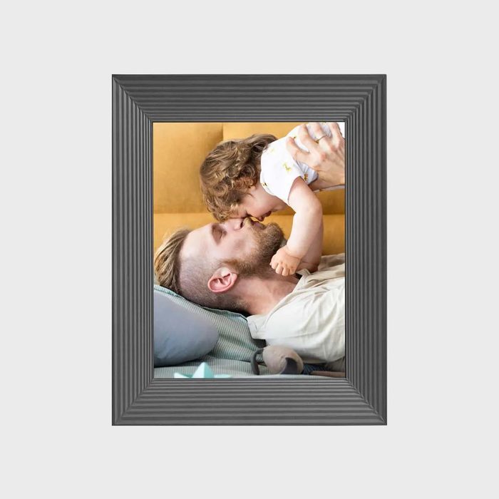 A child kisses a bearded man's nose, both lying on a couch. The photograph is framed with a ribbed black border.