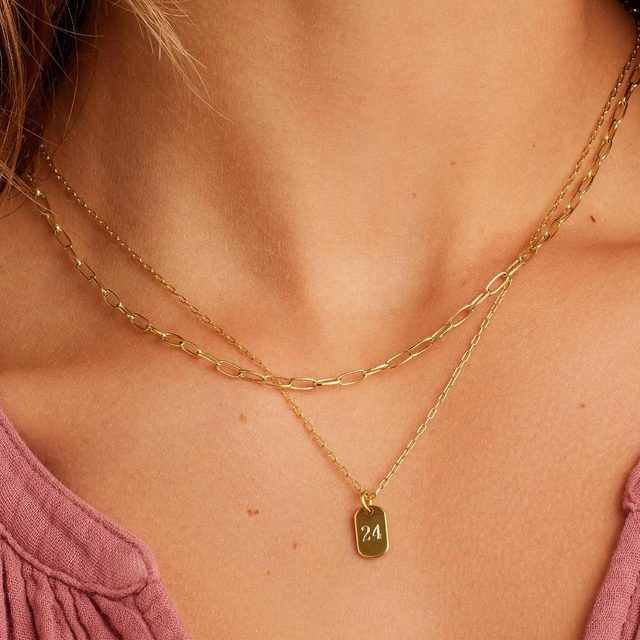 Gold necklaces rest on a person's neck, featuring a pendant with 
