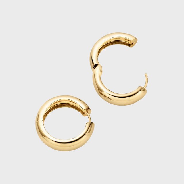 Gold hoop earrings lie open on a plain light background, showcasing their shiny, smooth surface and clasp mechanism.