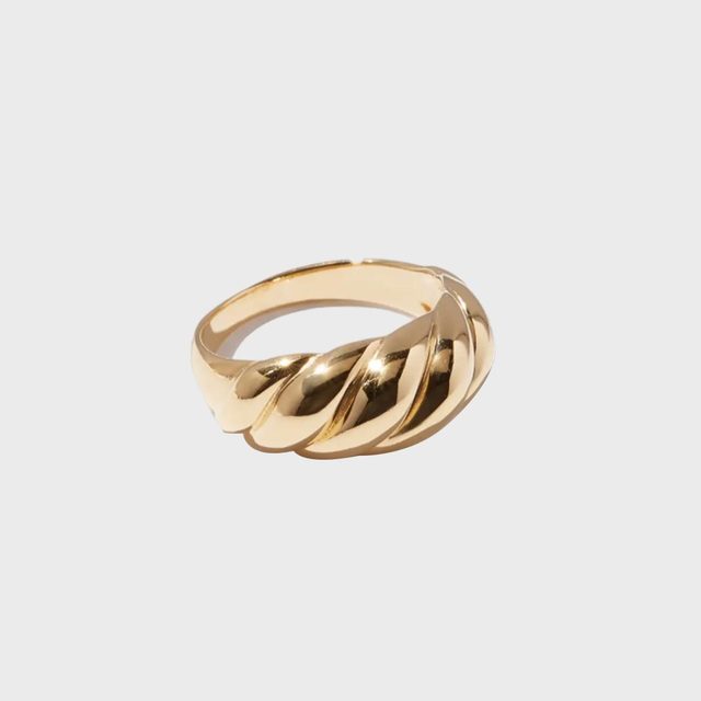 Gold ring features a twisted design, resting on a plain, light gray background.