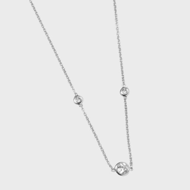 Necklace features spaced round diamond-like stones on a delicate silver chain, set against a plain white background.