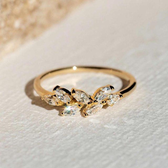 Gold ring featuring marquise-cut gemstones, resting on a textured surface, illuminated by soft light.