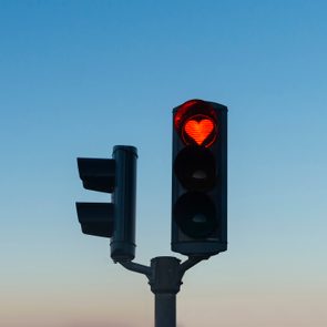 Traffic light displays a red heart icon; stands against a clear blue sky background.