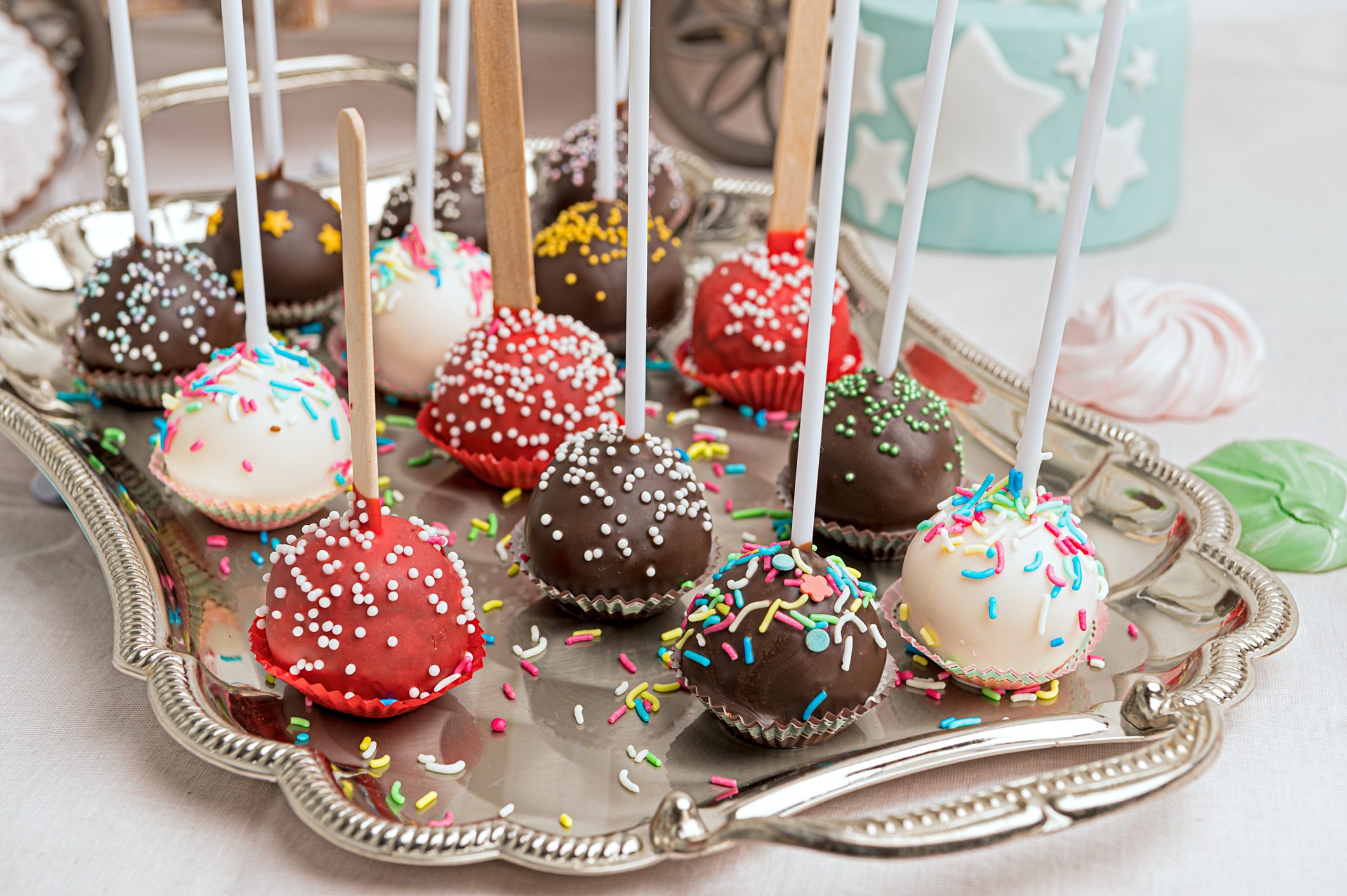 Cake pops with colorful sprinkles stand on sticks, arranged on a silver platter in a decorative setting.