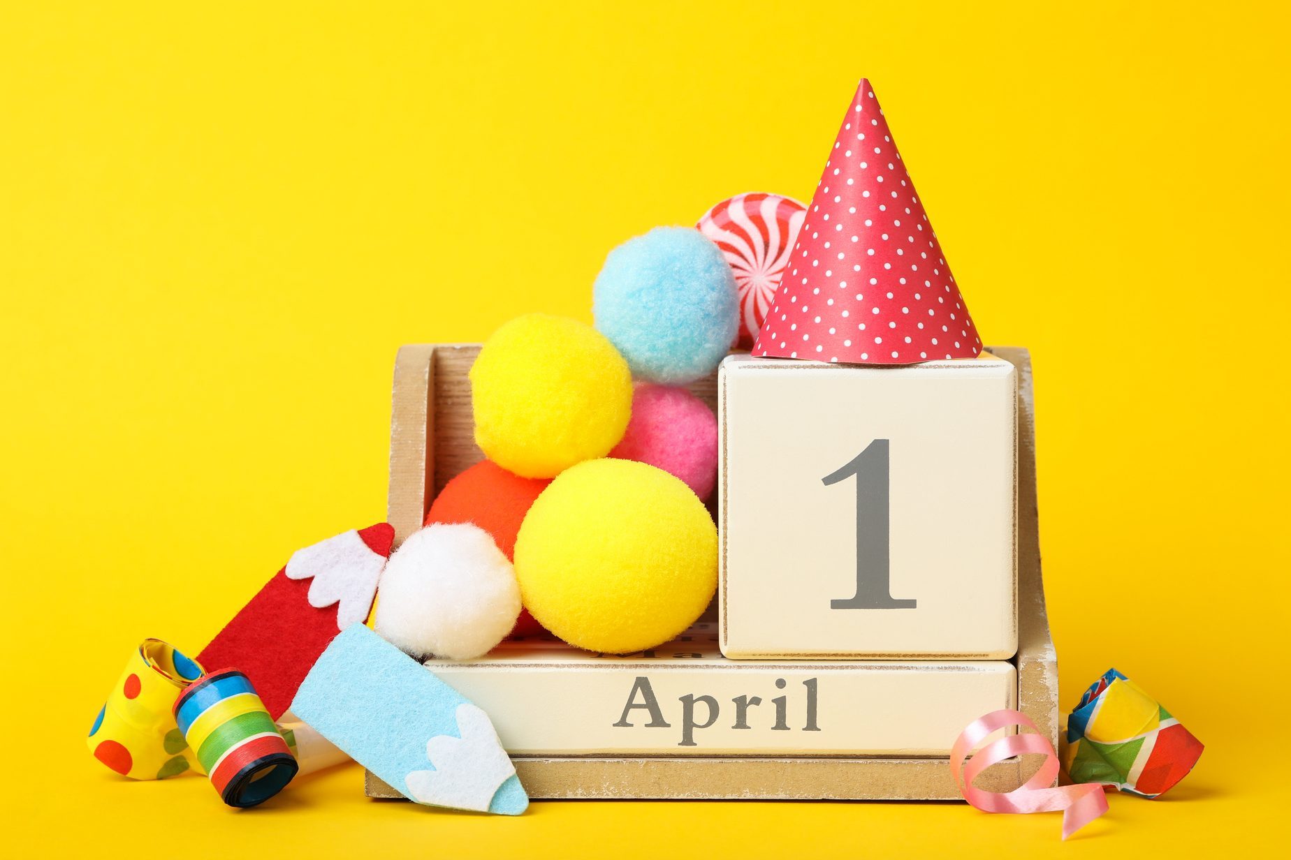 Wooden block calendar and party decor on yellow background. April fool's day