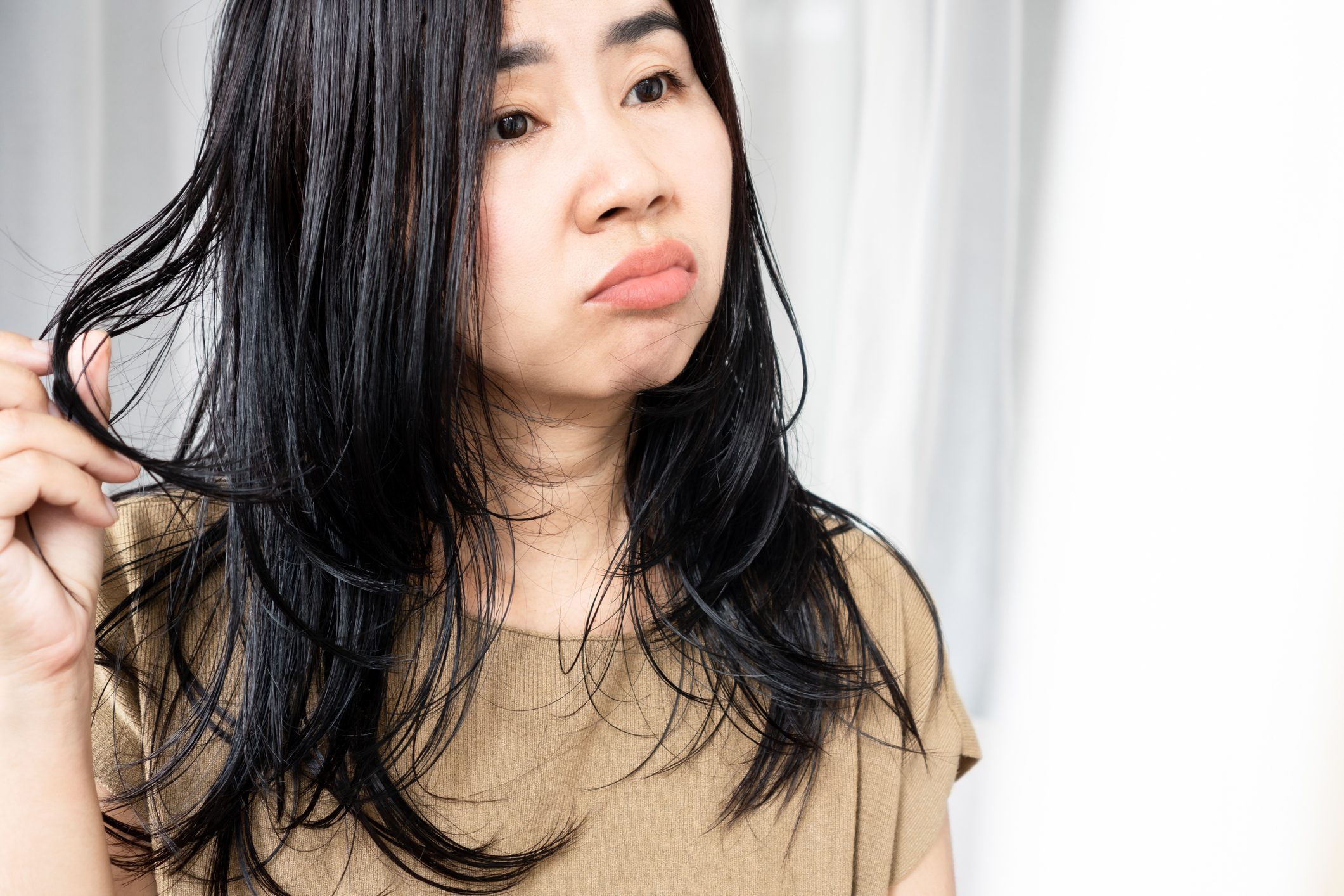 Asian woman have problems with oily hair and thinning hair looking at the mirror