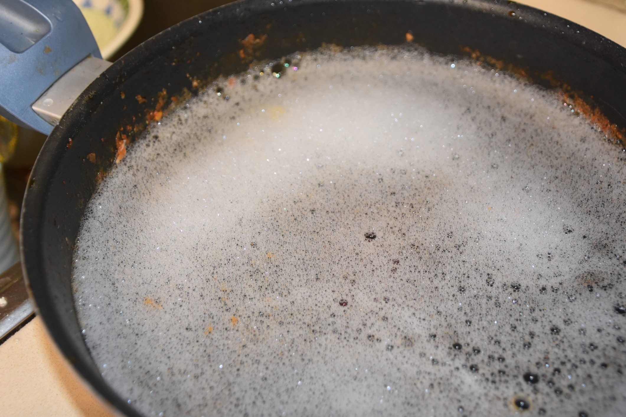 A frying pan holds soapy water with foam covering the surface, resting on a kitchen counter.