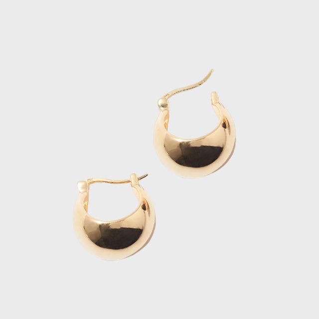 Gold hoop earrings lie on a plain surface, reflecting light subtly, creating a sleek and elegant appearance.