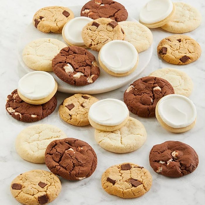 Cookies are scattered on a marble surface, featuring vanilla, chocolate chunks, and frosted varieties, creating a diverse and appetizing assortment.
