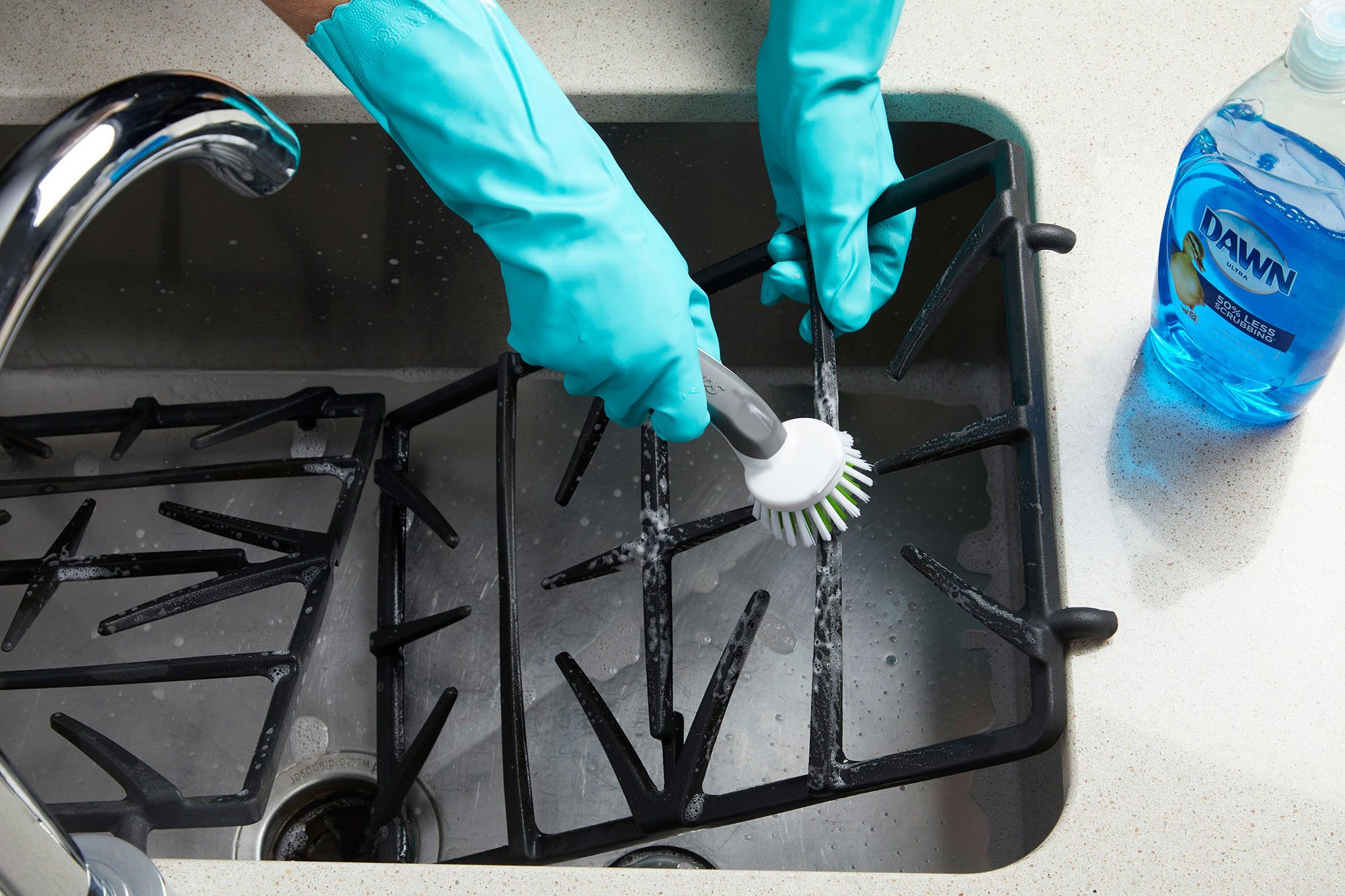 hands scrubbing the gas stove grates in a kitchen sink