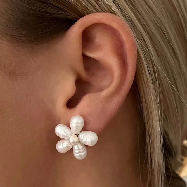 Earring shaped like a flower with pearl petals, worn on an ear, surrounded by blonde hair.