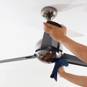 Person cleaning a modern ceiling fan with a cloth, focusing on the blades. The fan is mounted on a white ceiling.