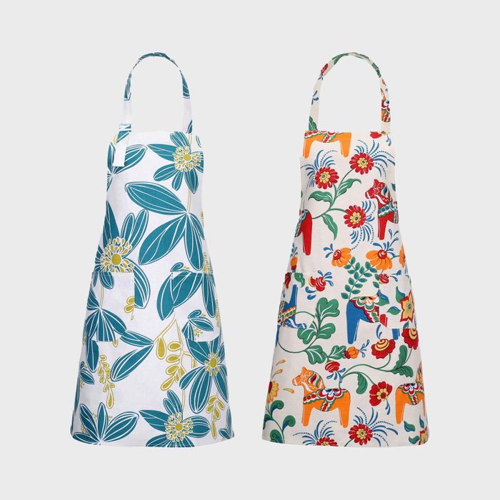 Two aprons display vibrant floral and abstract animal patterns, hanging side by side on a plain light gray background.