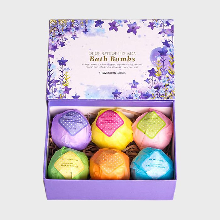 Box of colorful bath bombs displayed in purple packaging, with floral design lid. Text reads 